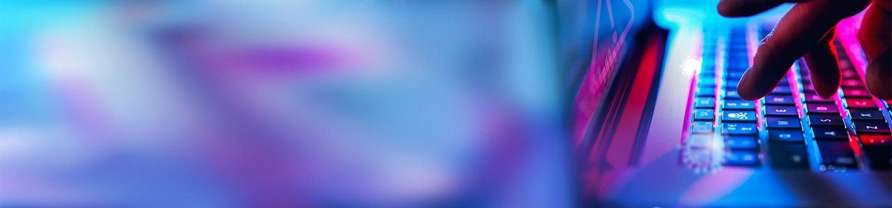 Eine Hand tippt auf einer Laptop-Tastatur mit leuchtend blauer und roter Hintergrundbeleuchtung